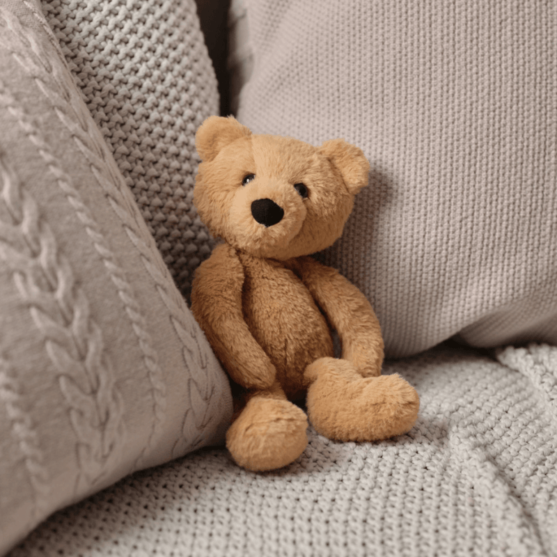 Charlie Bear oatmeal-brown plush teddy sitting between cushions on a sofa