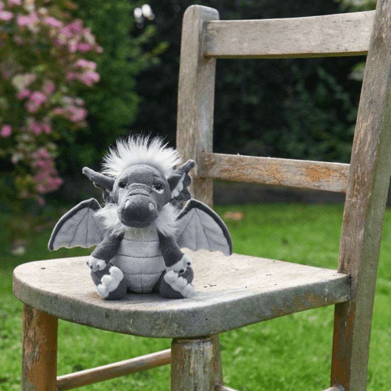 Soot Charlie Bears Cuddle Cubs dragon soft toy sitting on a wooden chair outdoors in a garden