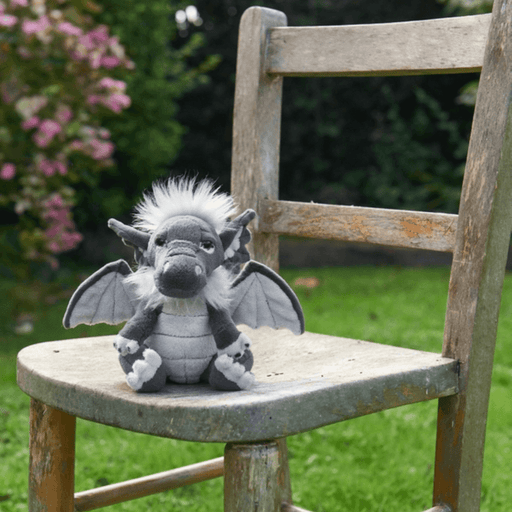 Soot Charlie Bears Cuddle Cubs dragon soft toy sitting on a wooden chair outdoors in a garden