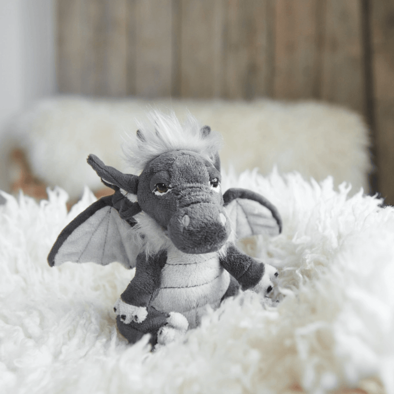 Soot Charlie Bears Cuddle Cubs dragon soft toy sitting on a fluffy white blanket with wings out