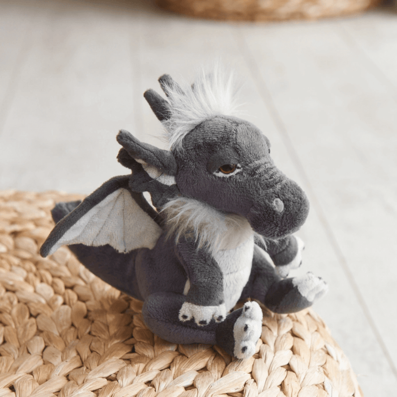 Soot Charlie Bears Cuddle Cubs dragon soft toy perched on a woven mat showing soft wings and fluffy crest