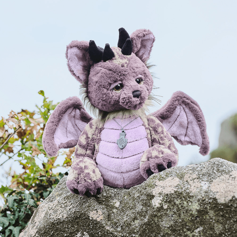 Charlie Bears Eragon mythical Tatzelwurm plush displayed outdoors on a stone wall with wings spread