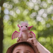 Charlie Bears Festoon dragon plush soft toy held outdoors, showing pink wings, fluffy white mane and sweet face