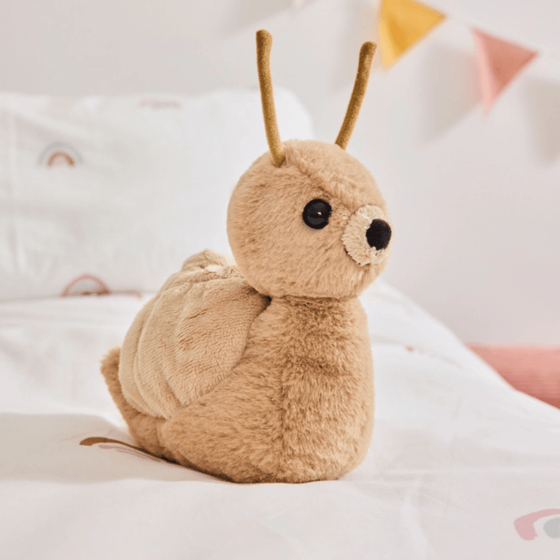 Charlie Bears Saffy Snail oatmeal-brown plush soft toy sitting on a child’s bed