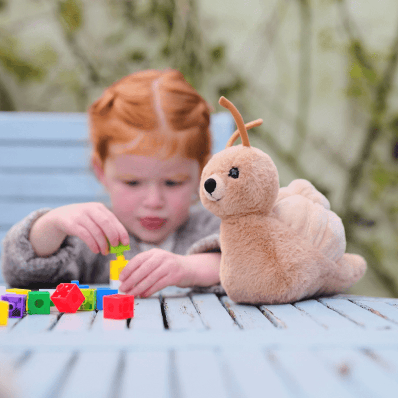 Child playing beside Charlie Bears Saffy Snail plush soft toy