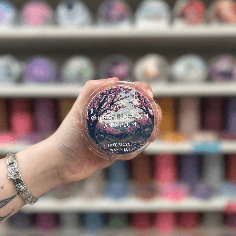 Cherry Blossom and Plum wax melt pot held in hand in front of a colourful wax melt display