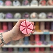 Soft pink segmented wax melt held in hand with colourful wax melts blurred behind
