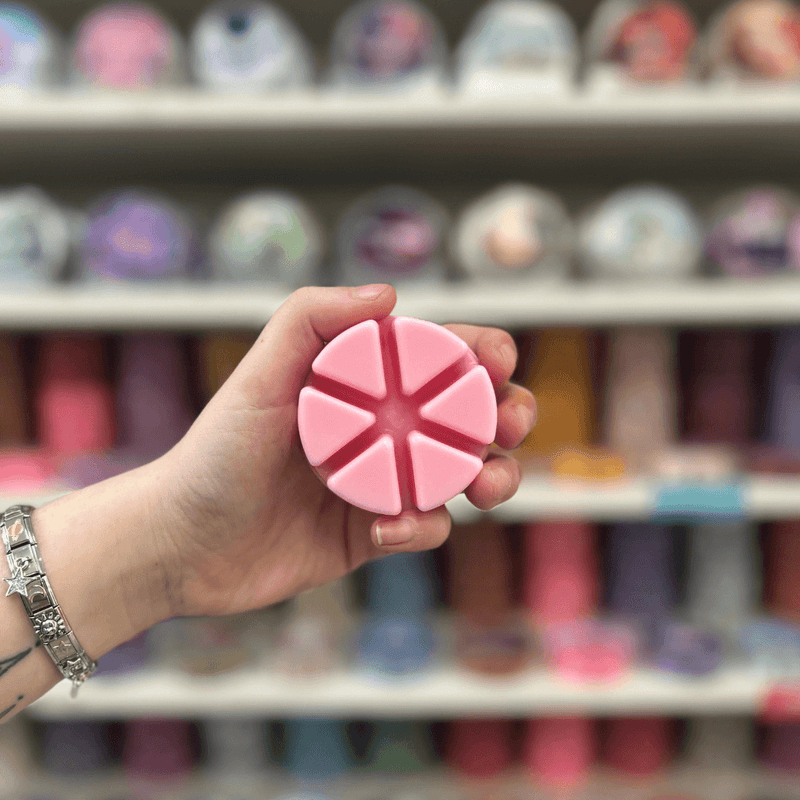 Soft pink segmented wax melt held in hand with colourful wax melts blurred behind