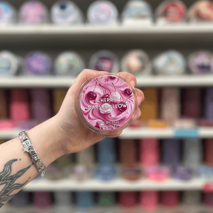 Cherry Marshmallow wax melt pot held in hand with colourful wax melt display in the background