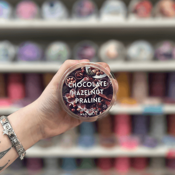Chocolate Hazelnut Praline wax melt pot held in hand with colourful wax melts blurred behind