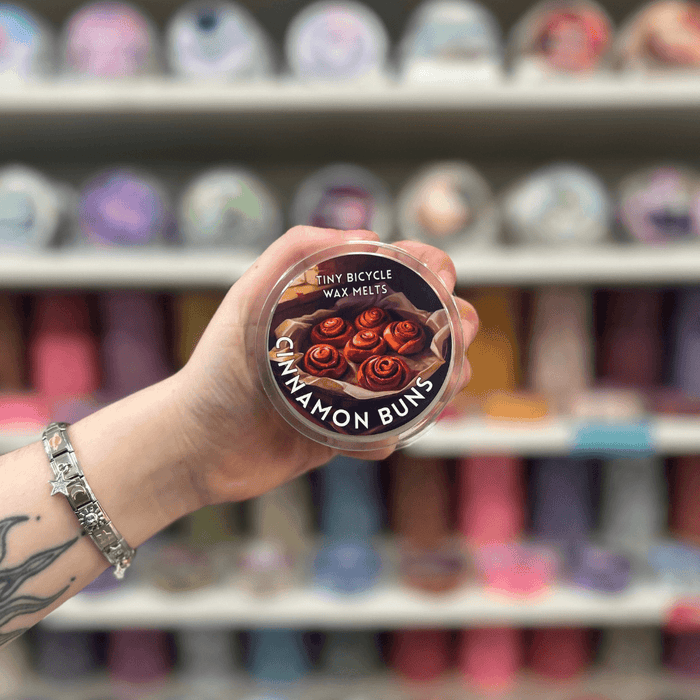 Cinnamon Buns wax melt pot held in hand with colourful wax melt display in the background