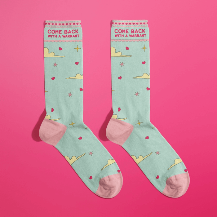 Mint green women’s crew socks with pink toes and heels, clouds, stars and hearts, slogan Come Back With A Warrant, on hot pink background.