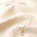 Delicate gold crescent moon necklace with crystal star details displayed on soft cream fabric, dainty celestial jewellery.