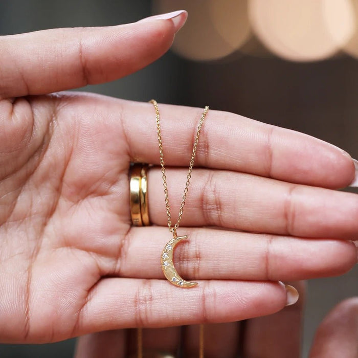 Gold crescent moon pendant with sparkling crystal stars shown in hand; small celestial necklace ideal for gifting.