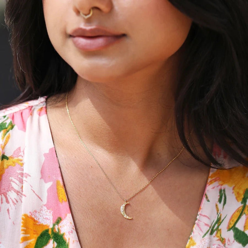 Model wearing a dainty gold crescent moon pendant with crystal stars; subtle everyday celestial necklace.