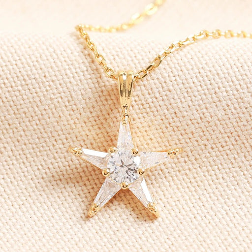 Gold star pendant necklace set with clear crystals on a fine chain, close-up of celestial jewellery piece on neutral fabric.