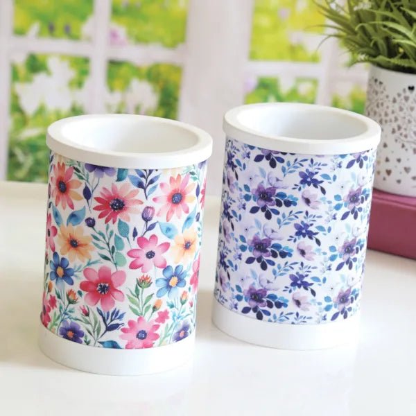Two electric wax melt burners in a styled setting, one with a daisy floral pattern and one with a blue floral pattern.