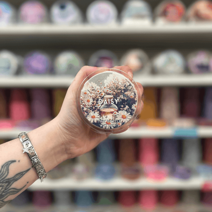 Daisy wax melt pot held in hand with colourful wax melt display in the background