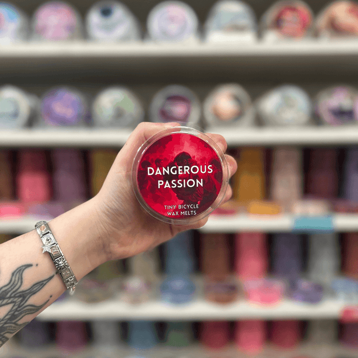 Dangerous Passion wax melt pot held in hand with colourful wax melt display in the background