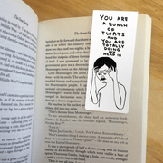 Magnetic bookmark clipped inside an open novel, showing Shrigley’s stressed figure and rude slogan.
