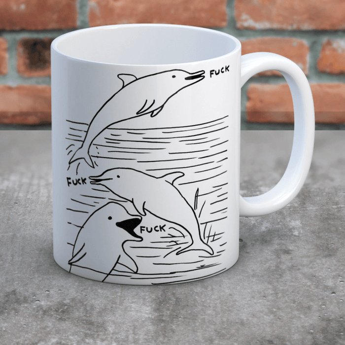 Swearing Dolphins mug on concrete surface against brick wall; wrap-around dolphin artwork clearly visible.
