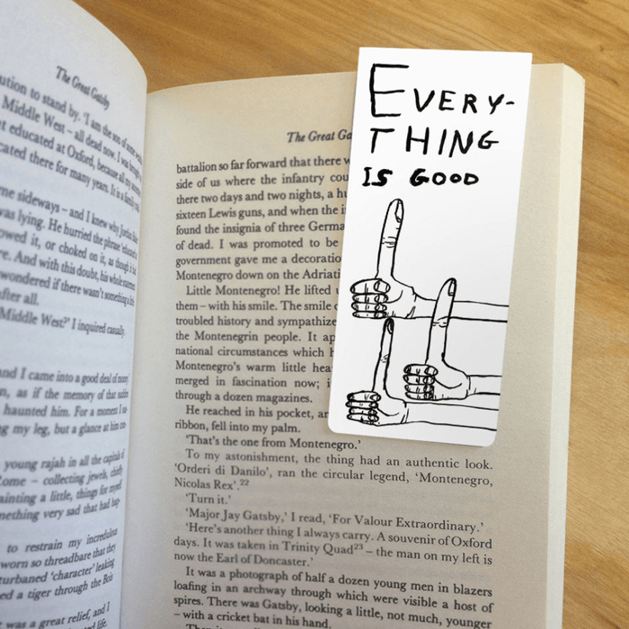 Magnetic bookmark clipped inside an open novel, showing thumbs-up artwork and slogan “Everything is good”.
