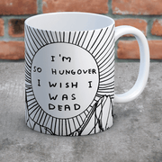 Hungover mug on concrete surface against brick wall; bold sunburst design clearly visible.
