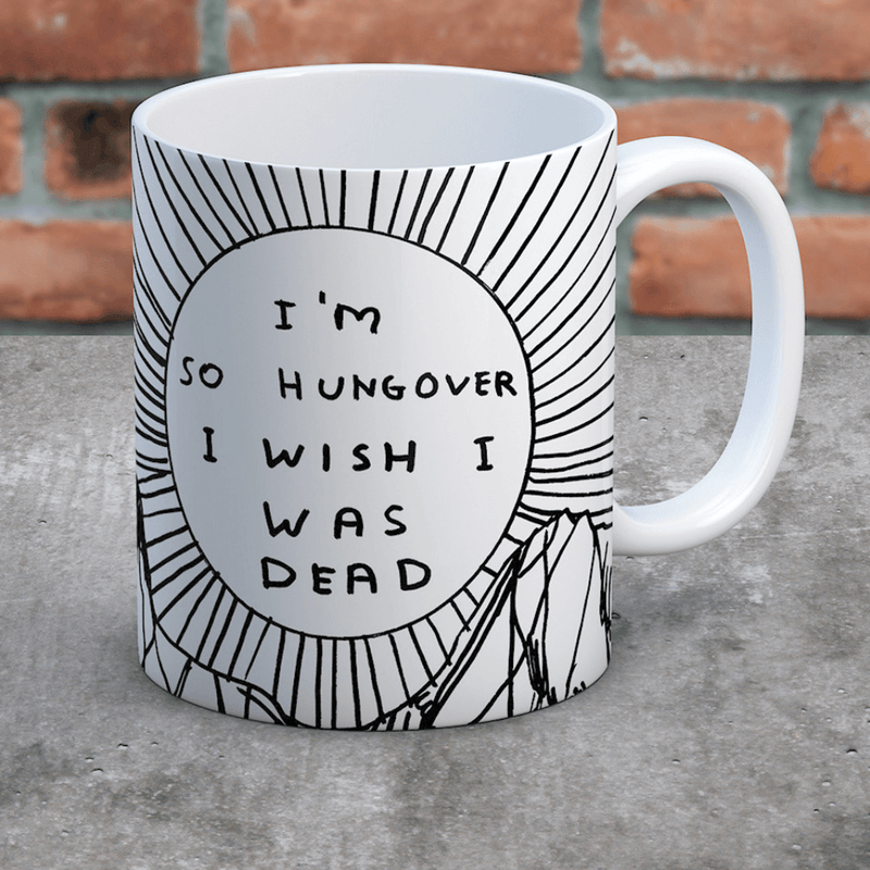 Hungover mug on concrete surface against brick wall; bold sunburst design clearly visible.
