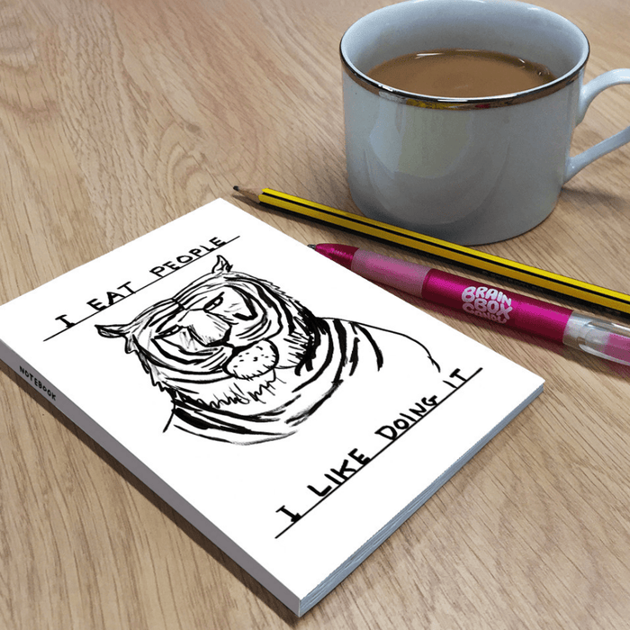 Lifestyle photo: humourous tiger notebook on desk beside pencil, pen and cup of tea.

