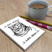 Lifestyle photo: humourous tiger notebook on desk beside pencil, pen and cup of tea.


