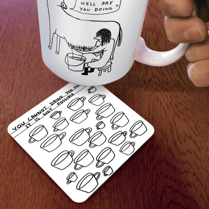 Too Much Tea coaster on wooden table under illustrated mug; cup pattern and humorous slogan visible at an angle.


