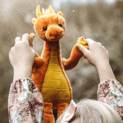 Diamonds orange dragon teddy from Bearhouse by Charlie Bears 2025 held up by hands outdoors, showing plush face and golden belly