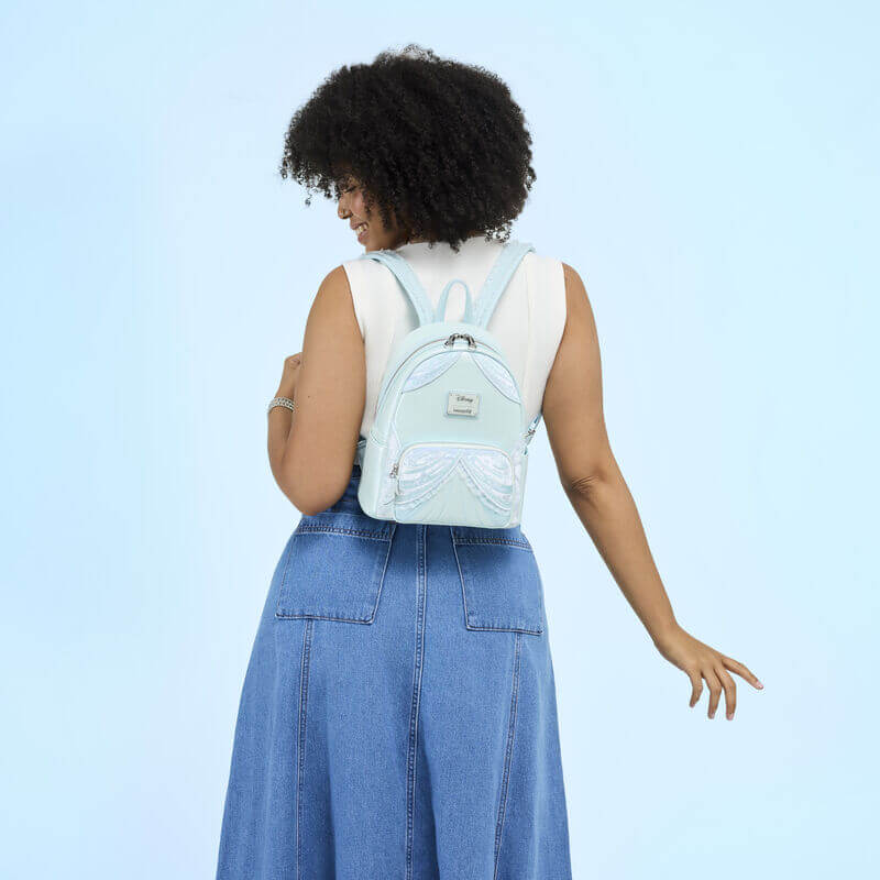 Model wearing pastel blue Cinderella Loungefly Back Pack bag with shimmering drape detail and glass‑slipper zip, rear view.	