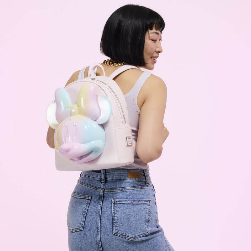 Model wearing pastel pink Minnie Tie‑Dye Loungefly Back Pack; large rainbow 3D Minnie face on back.	