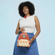 Model holding coral Disney Moana Loungefly Back Pack bag; tribal prints, cream floral pocket and aqua Heart of Te Fiti charm.	
