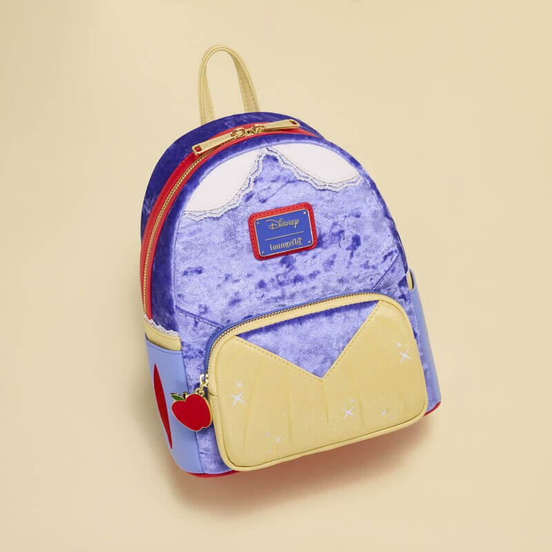 Velvet blue Snow White Loungefly Back Pack bag with yellow bodice pocket and red apple zip, flat‑lay on cream backdrop.	