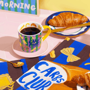 Eleanor Bowmer Carbs Club mug styled with croissants and colourful breakfast accessories