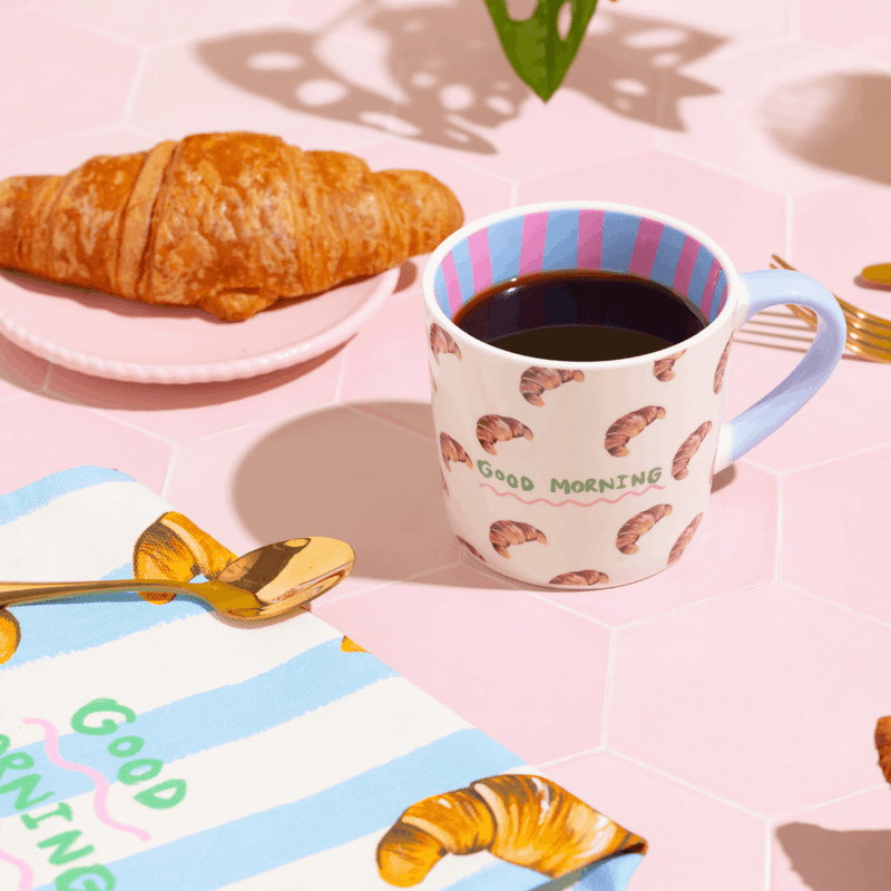Eleanor Bowmer Good Morning Croissant mug styled with coffee and a fresh croissant