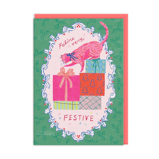 Green holly-bordered Christmas card with pink cat climbing stacked presents; hand-lettered text reads Feline Very Festive; A6, blank inside, coral envelope by Emily Taylor