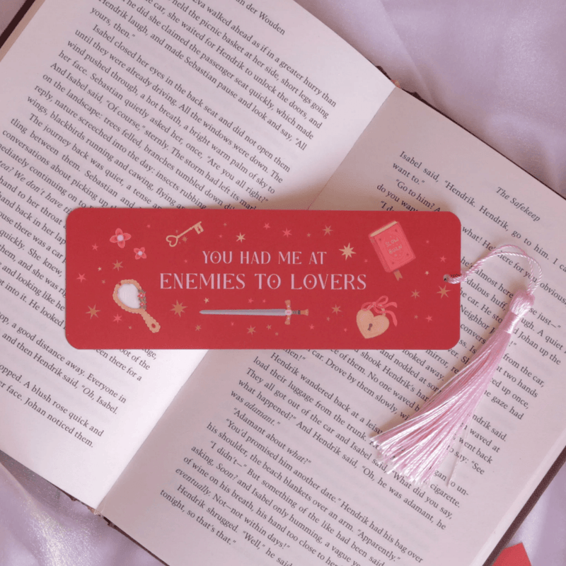 Enemies to Lovers romantasy bookmark with pink tassel inside an open book