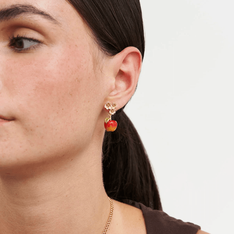 Close-up of a red apple drop earring with three gold and white blossoms worn on the ear