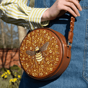 Fable England Bumble Circle Bag carried against blue denim showing the embroidered bee design