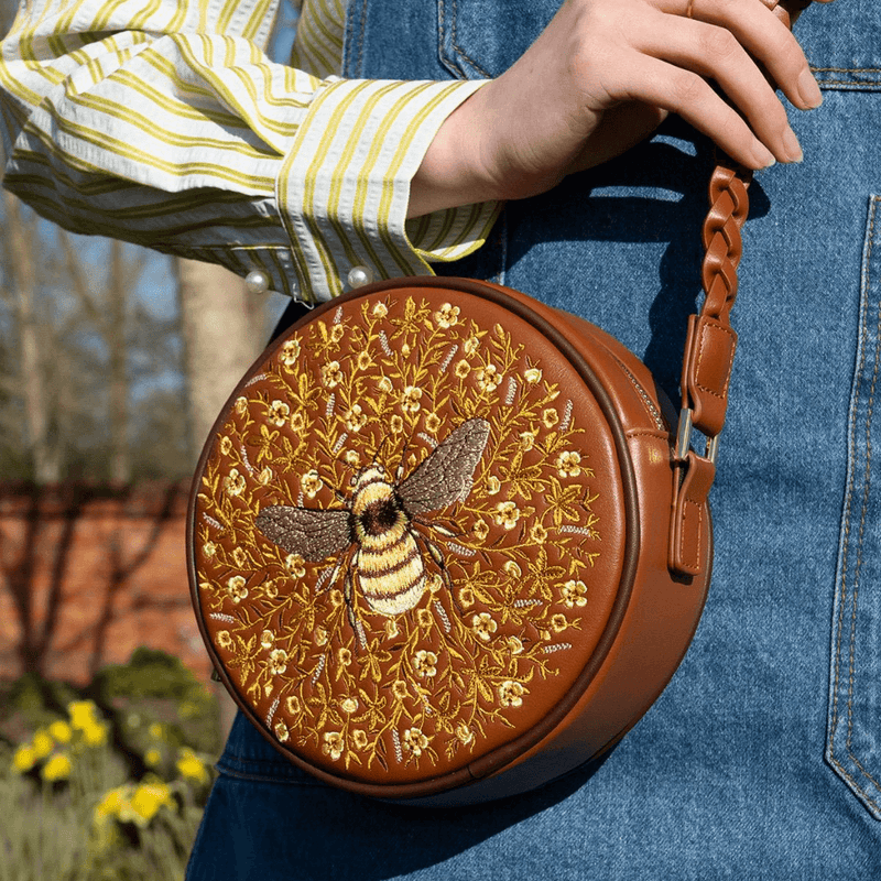 Fable England Bumble Circle Bag carried against blue denim showing the embroidered bee design