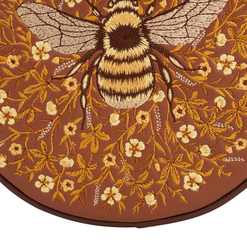 Close-up of embroidered bumblebee with striped body and detailed wings surrounded by golden wildflowers