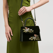Model carrying green velvet Fable England wren handbag with crossbody strap and matching green dress