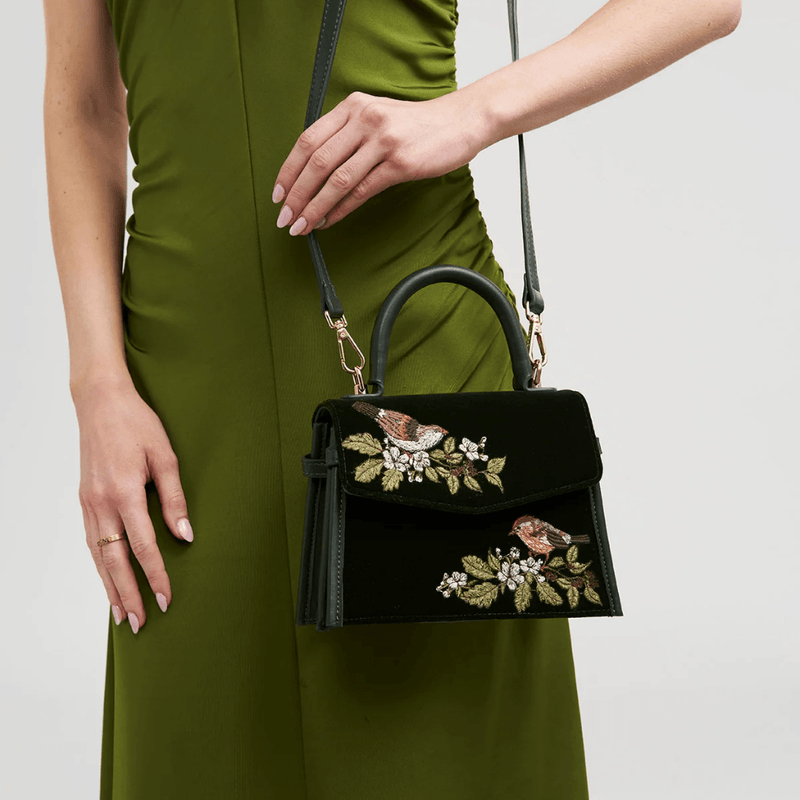 Model carrying green velvet Fable England wren handbag with crossbody strap and matching green dress
