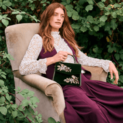Woman holding Fable England green velvet wren handbag while seated outdoors in a burgundy dress