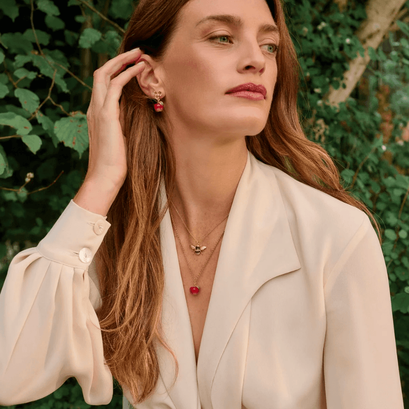 Woman wearing a gold Fable England apple pendant necklace layered with a bee necklace outdoors
