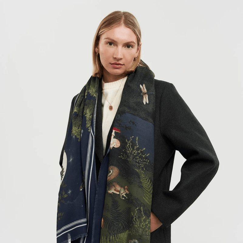 Model wearing the Fable England Woodland Meadow navy scarf draped over a dark coat