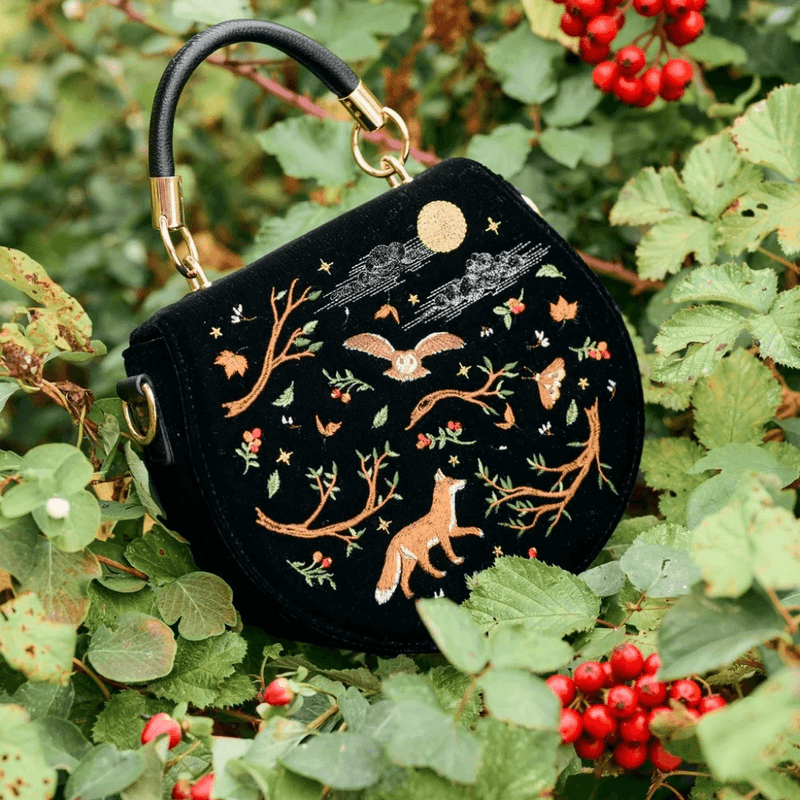 Fable England black fox and owl embroidered handbag displayed among green leaves and red berries